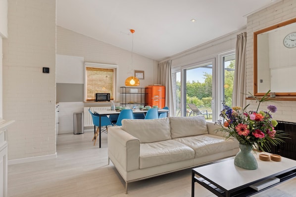 A modern living room with a sofa, a dining table, and a kitchen in the background.