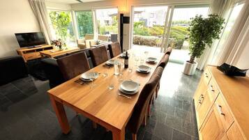 Un coin repas avec une table en bois dressée pour quatre personnes, un téléviseur et une vue sur le jardin grâce à de grandes fenêtres.
