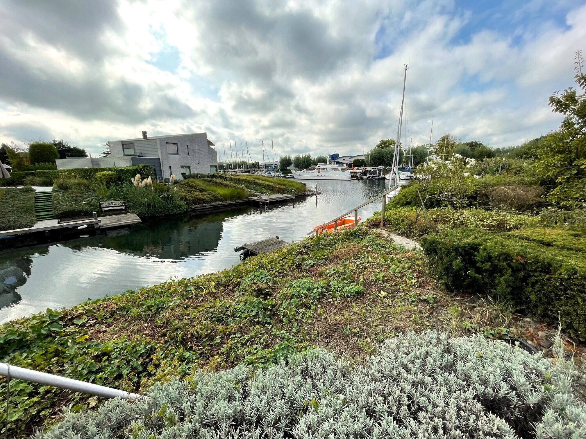 Een gracht met boten, een modern gebouw en weelderige begroeiing.