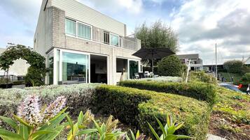 Een modern gebouw met grote ramen, een overdekt terras en verzorgde beplanting.