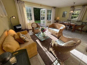 Un salon chaleureux avec un canapé, des fauteuils en osier, une table basse en verre et un coin repas comprenant une table et des chaises.