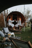 Una pareja sentada en una estructura circular de madera con una puerta, rodeada de muebles de exterior y plantas.