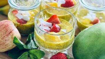 Een dessertopstelling met kleine glaasjes, gevuld met een gele smoothie, afgetopt met aardbeien en kokos.