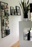Una habitación moderna con un estante metálico negro que contiene varios objetos, una planta en maceta y cuadros en la pared.