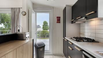 Een moderne keuken met een gasfornuis, houten kastjes, een afvalbak en een raam met gordijnen.