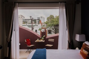 Quarto de hotel com varanda, uma cama, uma mesinha com um vaso de flores e uma cadeira.
