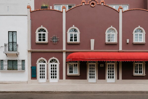Um edifício com toldo vermelho, janelas emolduradas por branco e varanda com grades de metal.