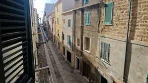 A narrow street with buildings featuring stone facades and multiple windows with shutters. - Room Cavour 80 (Alghero)