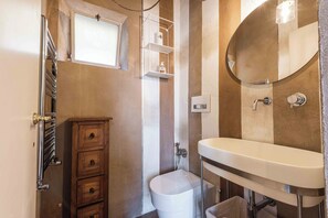 A bathroom with a white sink, a round mirror, a toilet, and a wooden cabinet with drawers. - Eleganza Antica by MMega (Florence)