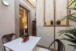 A small dining area with a white table and two chairs, a potted plant, and a window with decorative curtains. - Eleganza Antica by MMega (Florence)