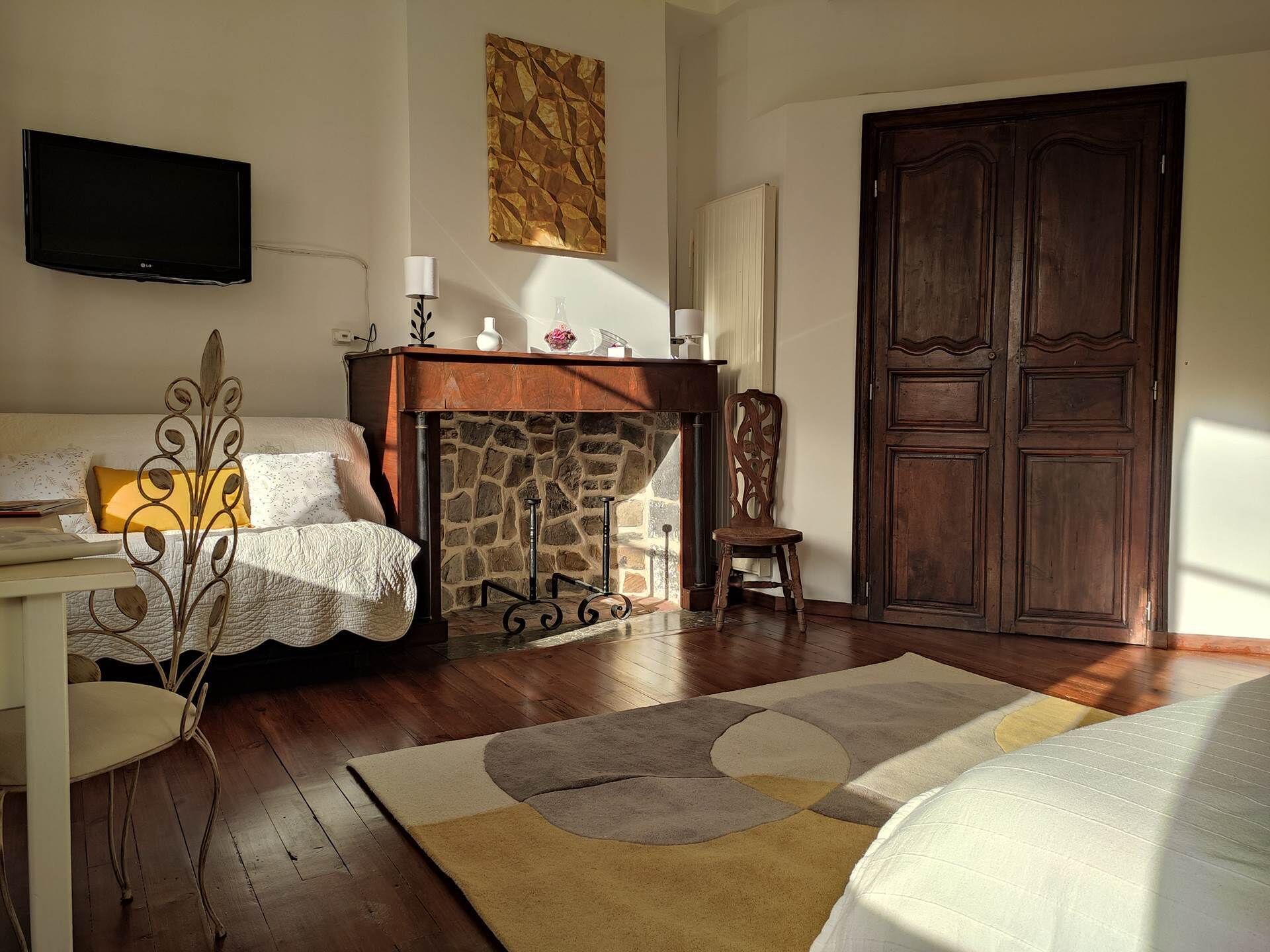 Une pièce avec une cheminée, une porte en bois, un téléviseur fixé au mur et un lit recouvert d’une couverture blanche.
