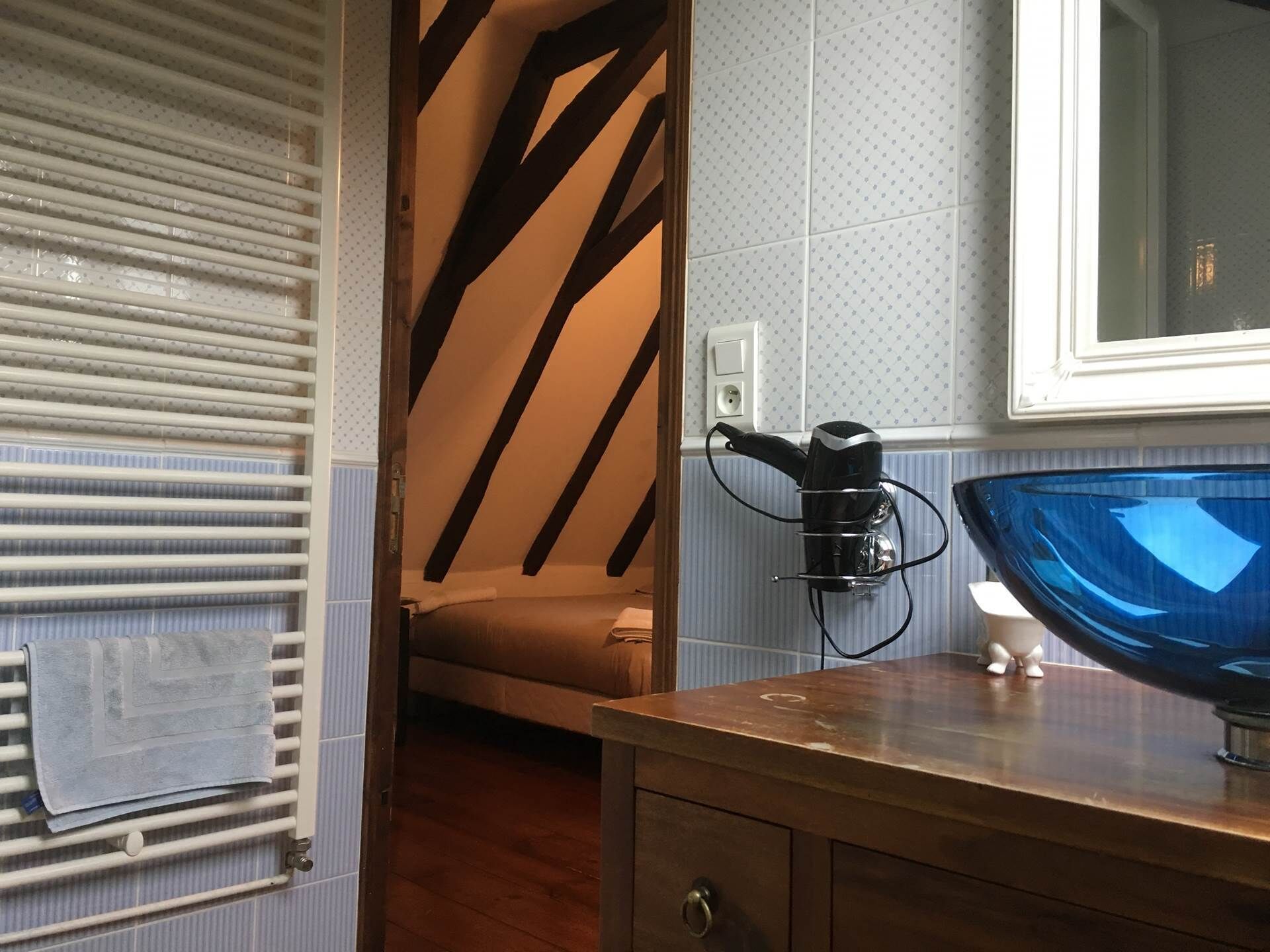 Ein Badezimmer mit Handtuchhalter, einem Handtuch, einem Fön, einem Waschbecken mit blauer Schüssel und einem Spiegel.