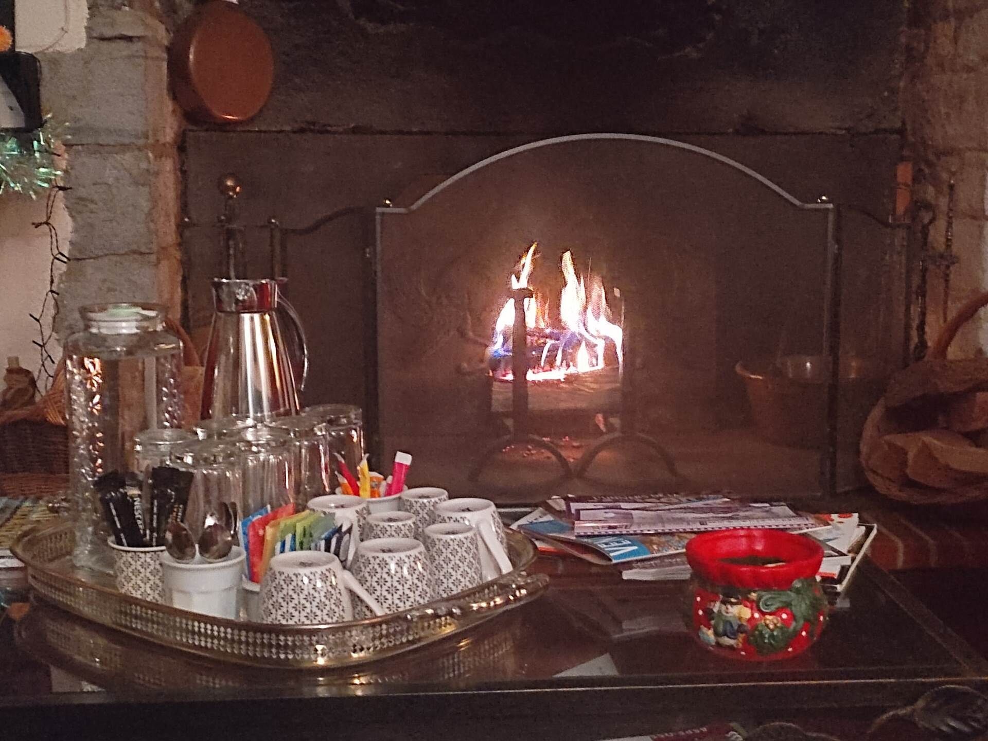 Un camino acceso, un vassoio con tazze e utensili, e una tazza rossa con decorazioni natalizie.