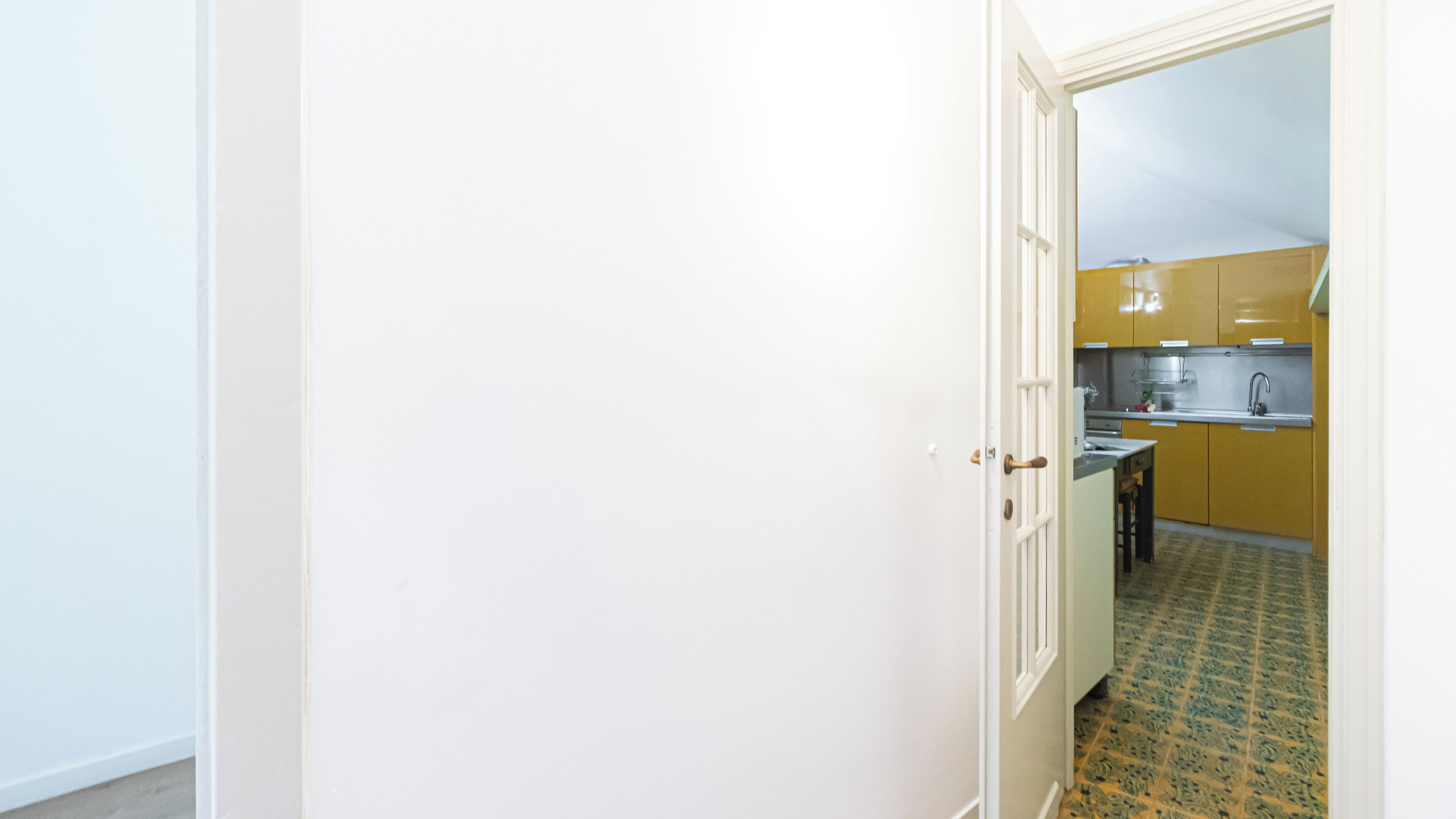A narrow hallway leading to a kitchen with yellow cabinets and a tiled floor.