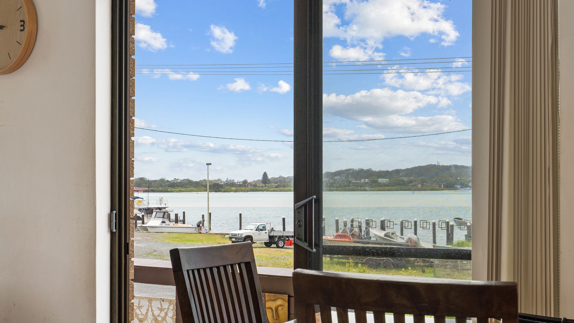 A room with a large window overlooking a lake, a chair, and a clock on the wall.
