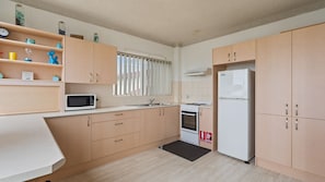 A compact kitchen with wooden cabinets, a microwave, a stove, and a refrigerator. - Dolphin Place 1 on the Tuncurry waterfront. (Tuncurry)