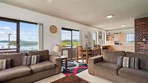 A spacious living area with two sofas, a dining table, and a kitchen in the background. - Dolphin Place 1 on the Tuncurry waterfront. (Tuncurry)