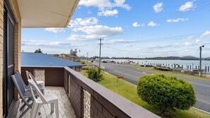 A balcony with a view of a waterfront road, a small garden, and a clear sky. - Dolphin Place 1 on the Tuncurry waterfront. (Tuncurry)