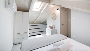 Une chambre avec un lit superposé, une lucarne, une petite table de chevet avec un panier, et un miroir au mur.