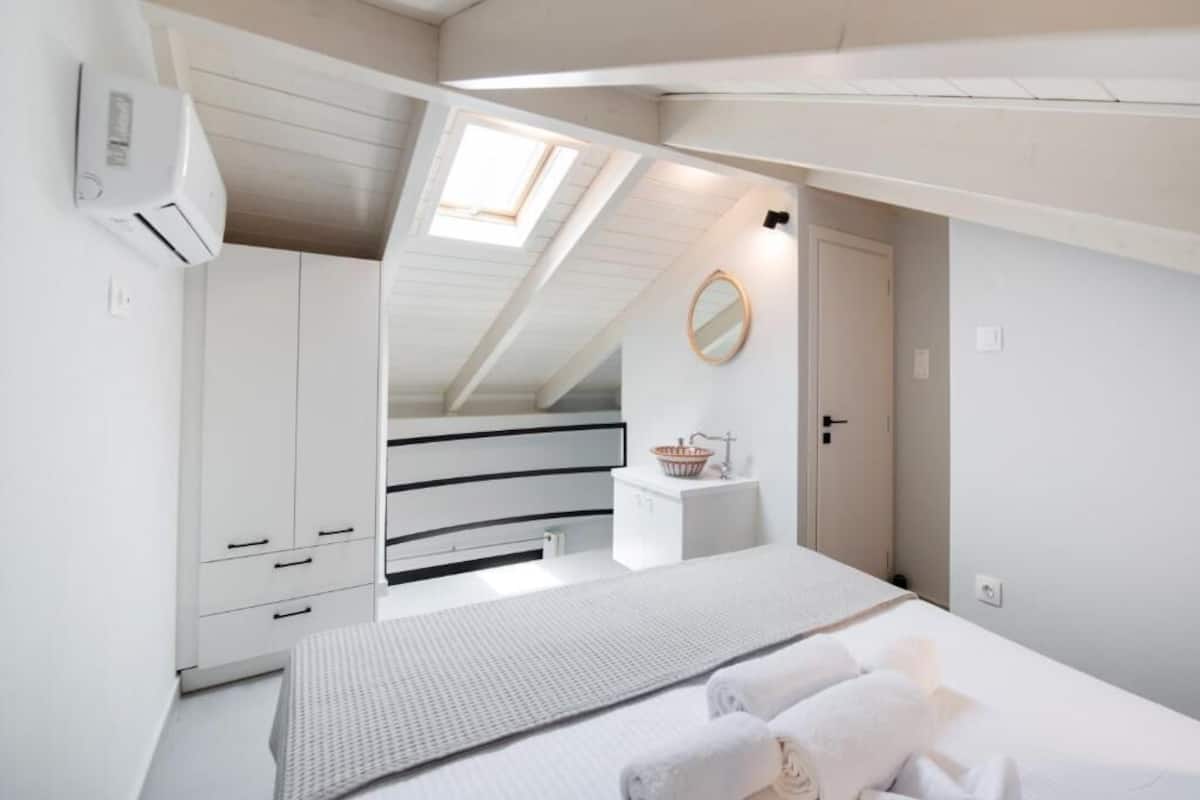 Une chambre avec un lit superposé, une lucarne, une petite table de chevet avec un panier, et un miroir au mur.