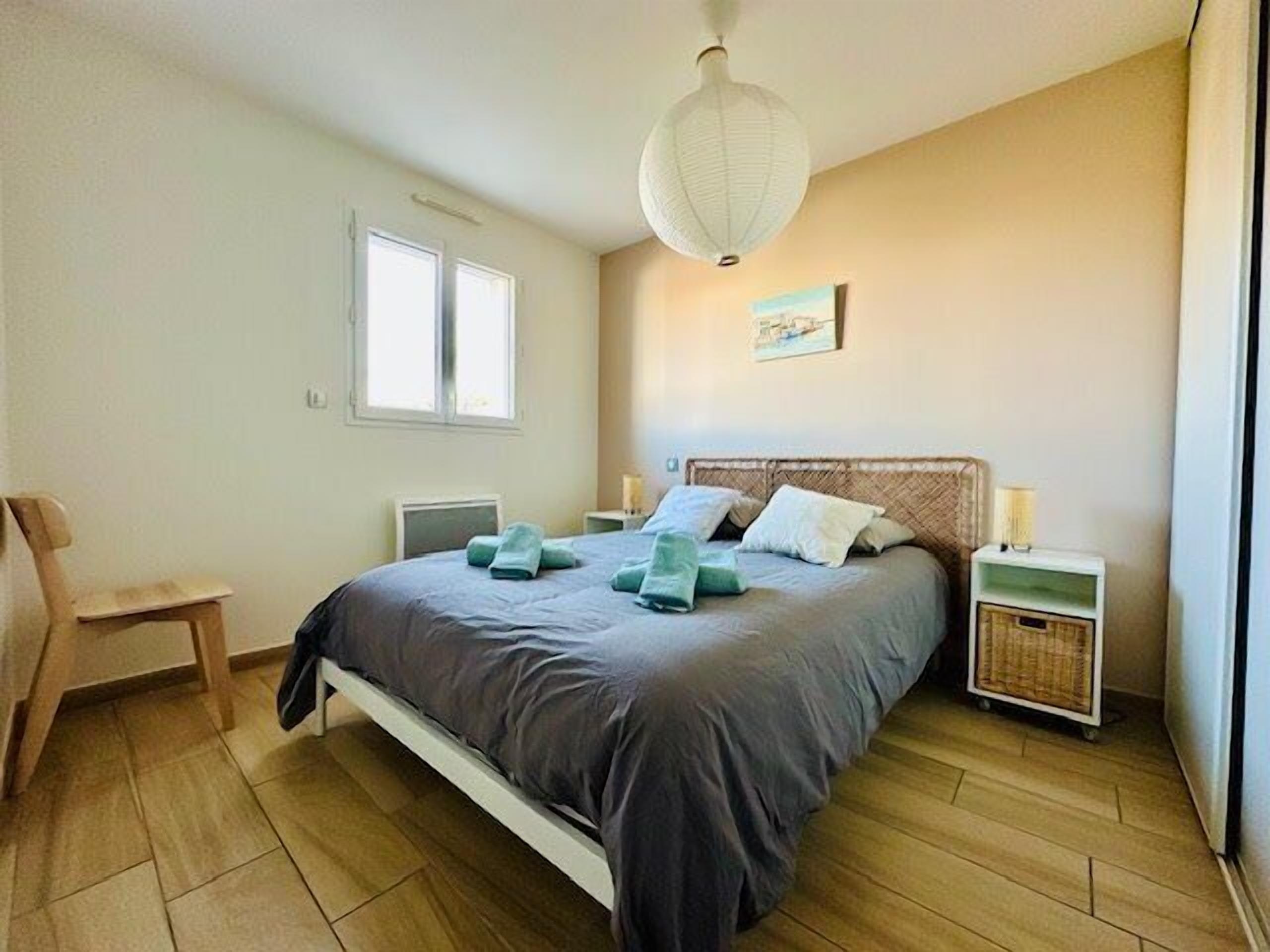 Une chambre à coucher comprenant un lit, des tables de chevet, une chaise, un luminaire suspendu et une fenêtre.