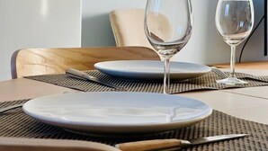 Una mesa de comedor con dos copas de vino vacías, un plato y un cuchillo sobre un mantel tejido.