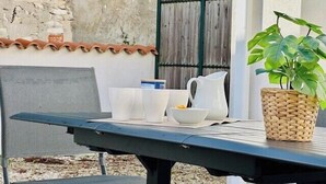 Una mesa de patio con una cesta trenzada, tazas blancas, una jarra y una silla.