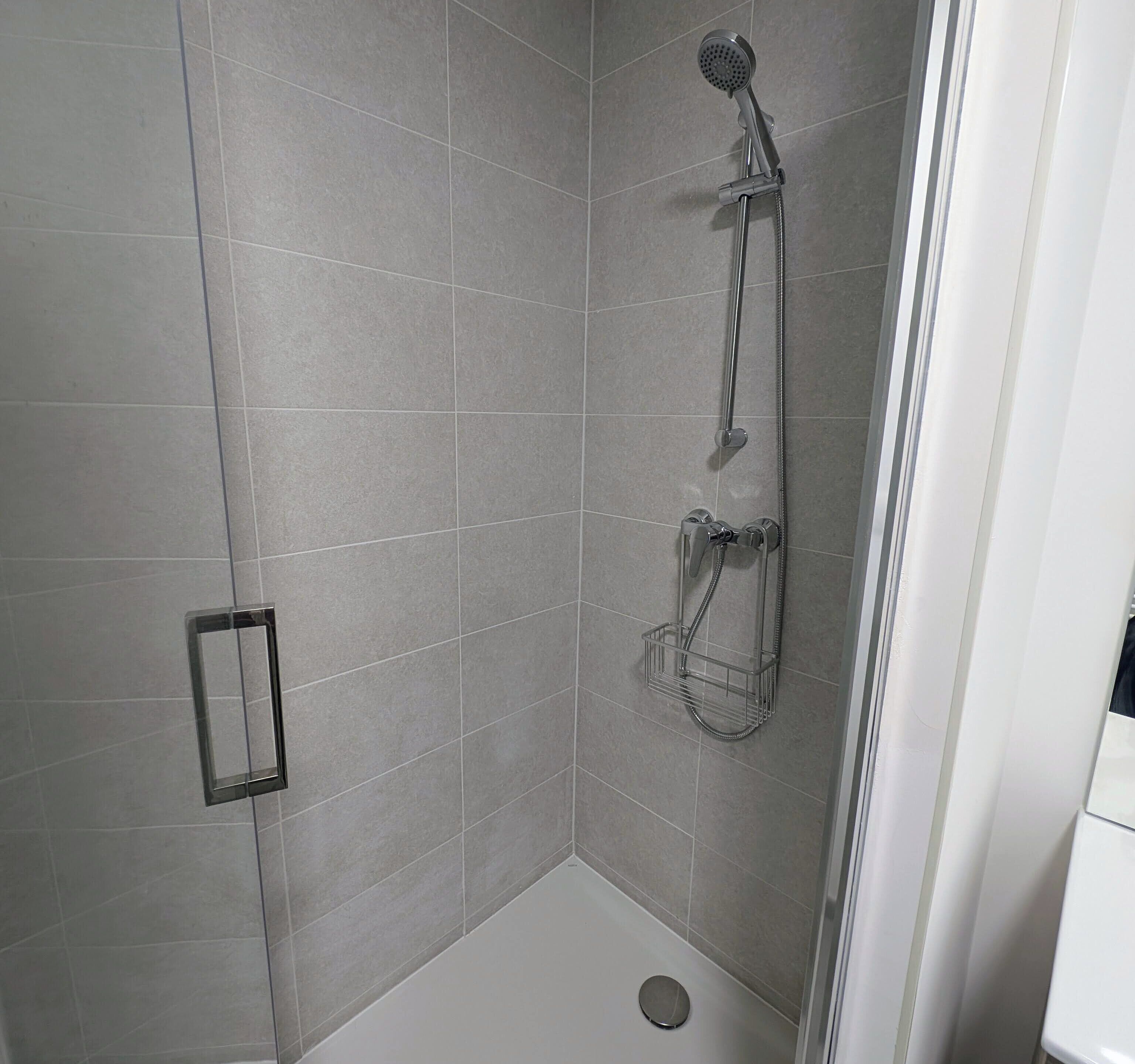 A corner shower with a handheld showerhead, a handheld shower attachment, and a wall-mounted showerhead.