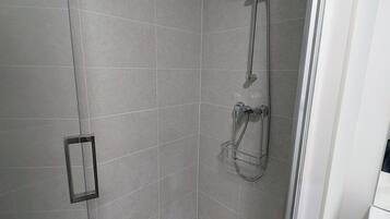 A corner shower with a handheld showerhead, a handheld shower attachment, and a wall-mounted showerhead.