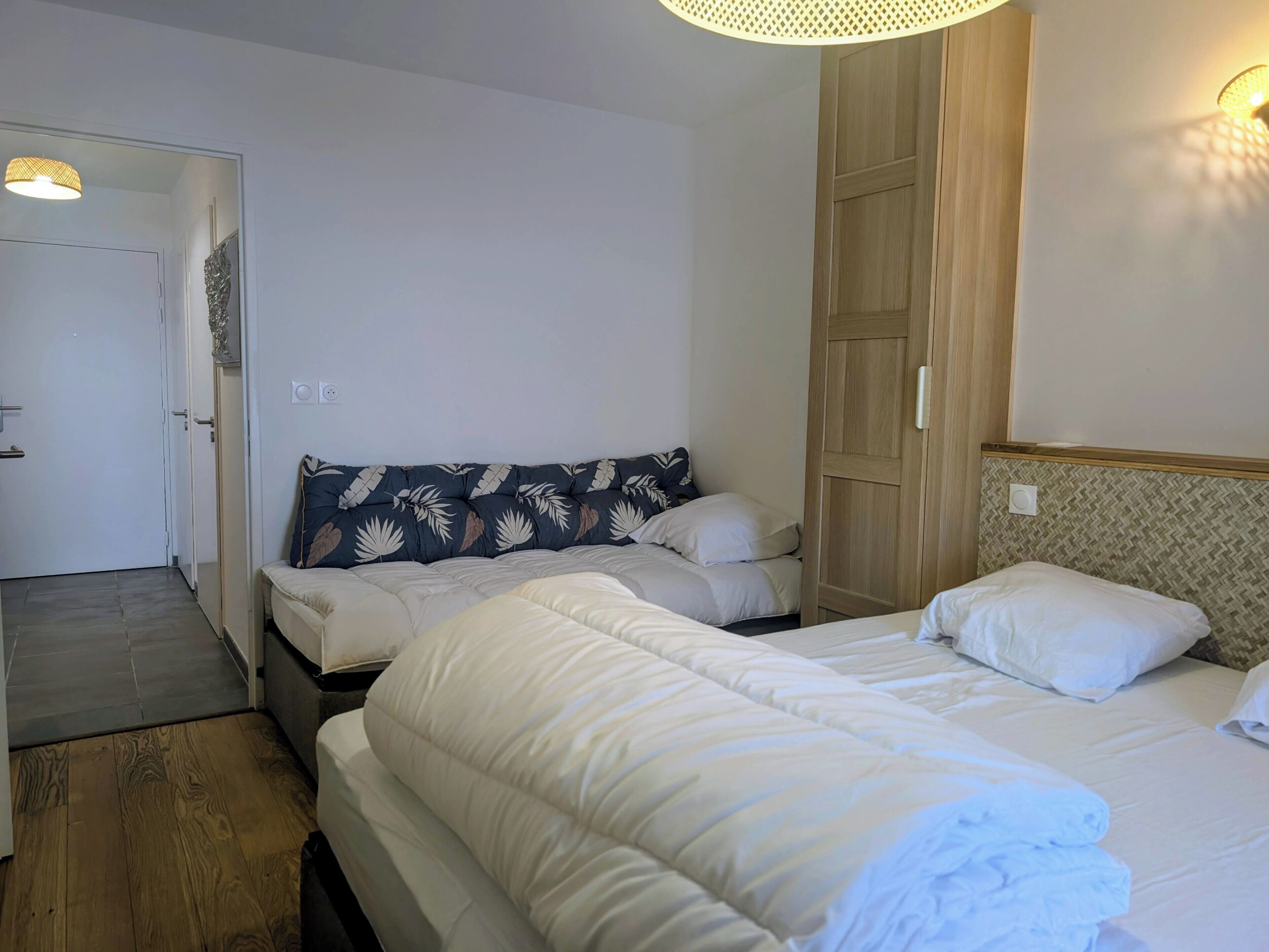 A bedroom with two beds, a wardrobe, and a door leading to another room.