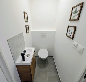 A compact bathroom with a white sink, wooden vanity, and a toilet. There are framed botanical prints on the walls. - Modern apartment close to the slopes in Briançon (Briançon)