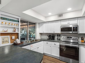 A modern kitchen with white cabinets, stainless steel appliances, and a black countertop. - Beautiful 2nd Floor Cottage at Hidden Dunes (Miramar Beach)