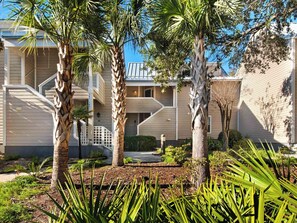 Um edifício residencial com área externa coberta, palmeiras e um jardim ajardinado.