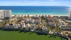 Vista aérea de uma área residencial costeira com imóveis à beira-mar, um porto de iates e um grande edifício de hotel.