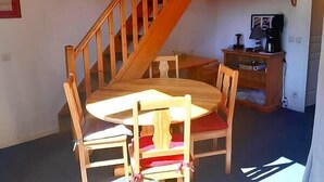 En matplats med ett träbord och stolar, en trappa och ett litet skåp med en lampa.