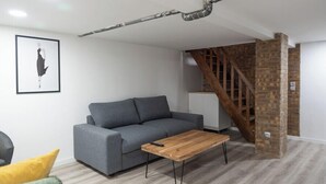 En stue med en grå sofa, et træsofabord og en trappe med blotlagte murstensvægge.