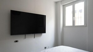 Et værelse med seng, tv på væggen, et vindue og en dør.