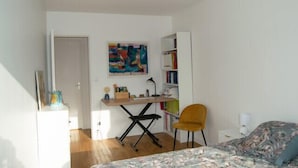 Un dormitorio con cama, escritorio, silla, estantería y puerta.