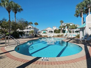 Una piscina con un cartello che indica divieto di tuffi, circondata da palme e case sulla spiaggia.