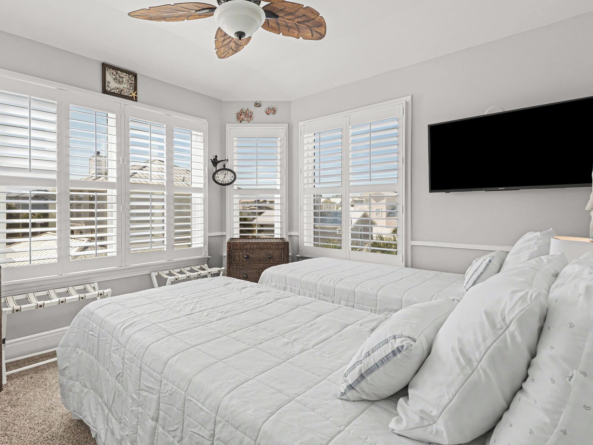 Une chambre avec deux lits, un ventilateur de plafond, une horloge et de grandes fenêtres équipées de volets.