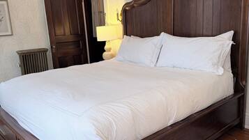 A large, dark wooden bed with white bedding in a room with patterned wallpaper and a wooden floor.