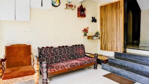 A living room with a sofa, a wooden chair, a clock, and a staircase leading to a dark room. - Super Hotel O Benaulim Beach Goa (Benaulim)