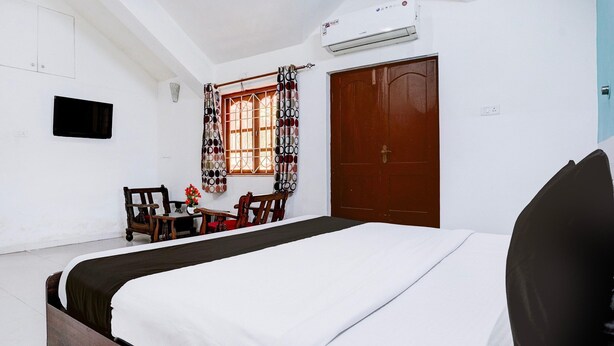 A hotel room with a large bed, a wooden desk, a chair, a window with patterned curtains, and a closed door. - Super Hotel O Benaulim Beach Goa (Benaulim)