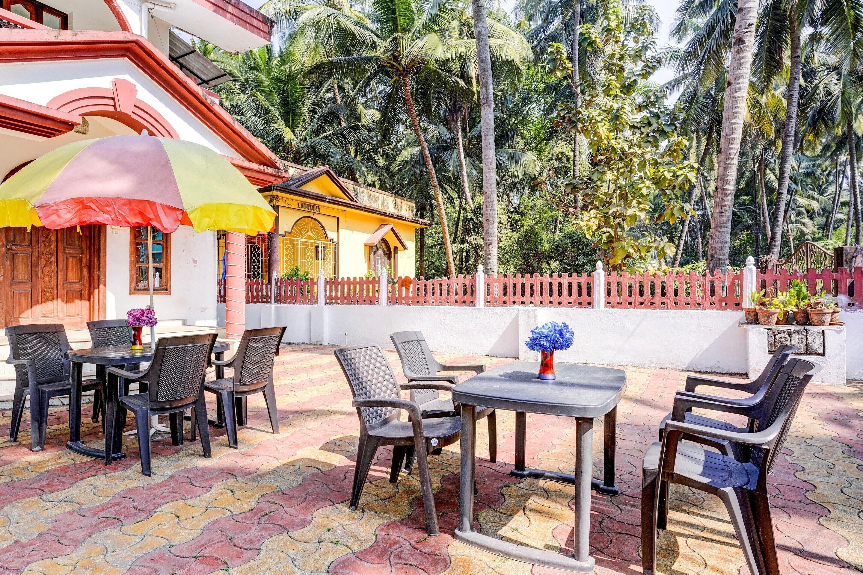 An outdoor seating area with tables and chairs, surrounded by a red fence and palm trees.