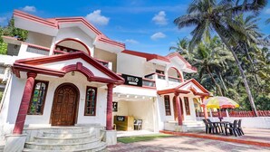 A hotel with a red and white facade, a signboard, and a seating area with an umbrella. - Super Hotel O Benaulim Beach Goa (Benaulim)
