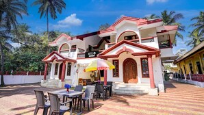A hotel with a balcony, outdoor seating area, and palm trees in the background. - Super Hotel O Benaulim Beach Goa (Benaulim)