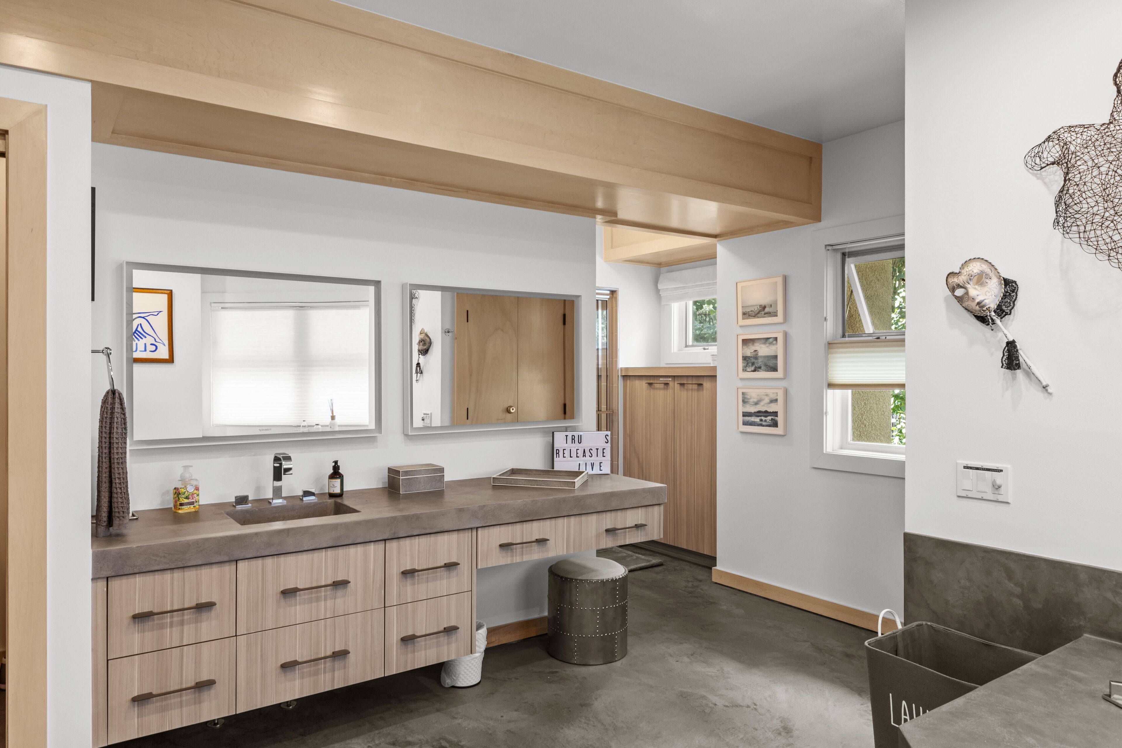 A modern bathroom with a large mirror, wooden vanity, and a window.