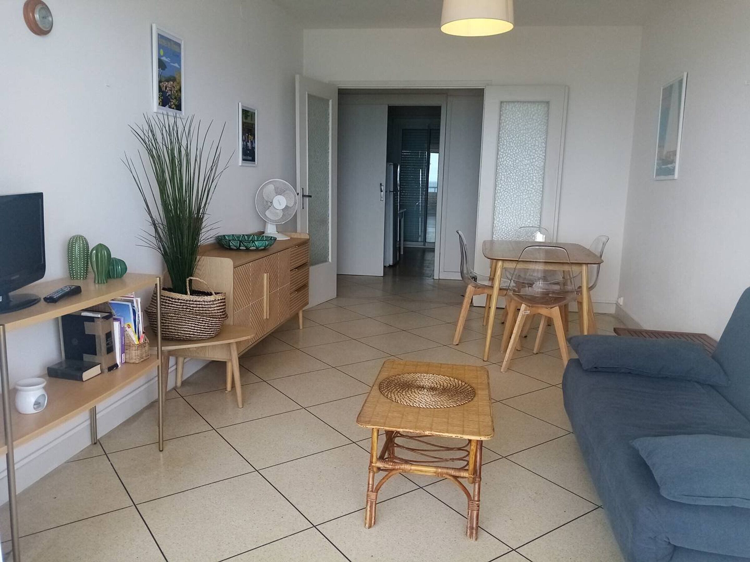 Uma sala de estar com sofá, mesinha, televisão e ventoinha.