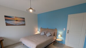 Un dormitorio con cama, mesita de noche, lámpara, un cuadro y una puerta.