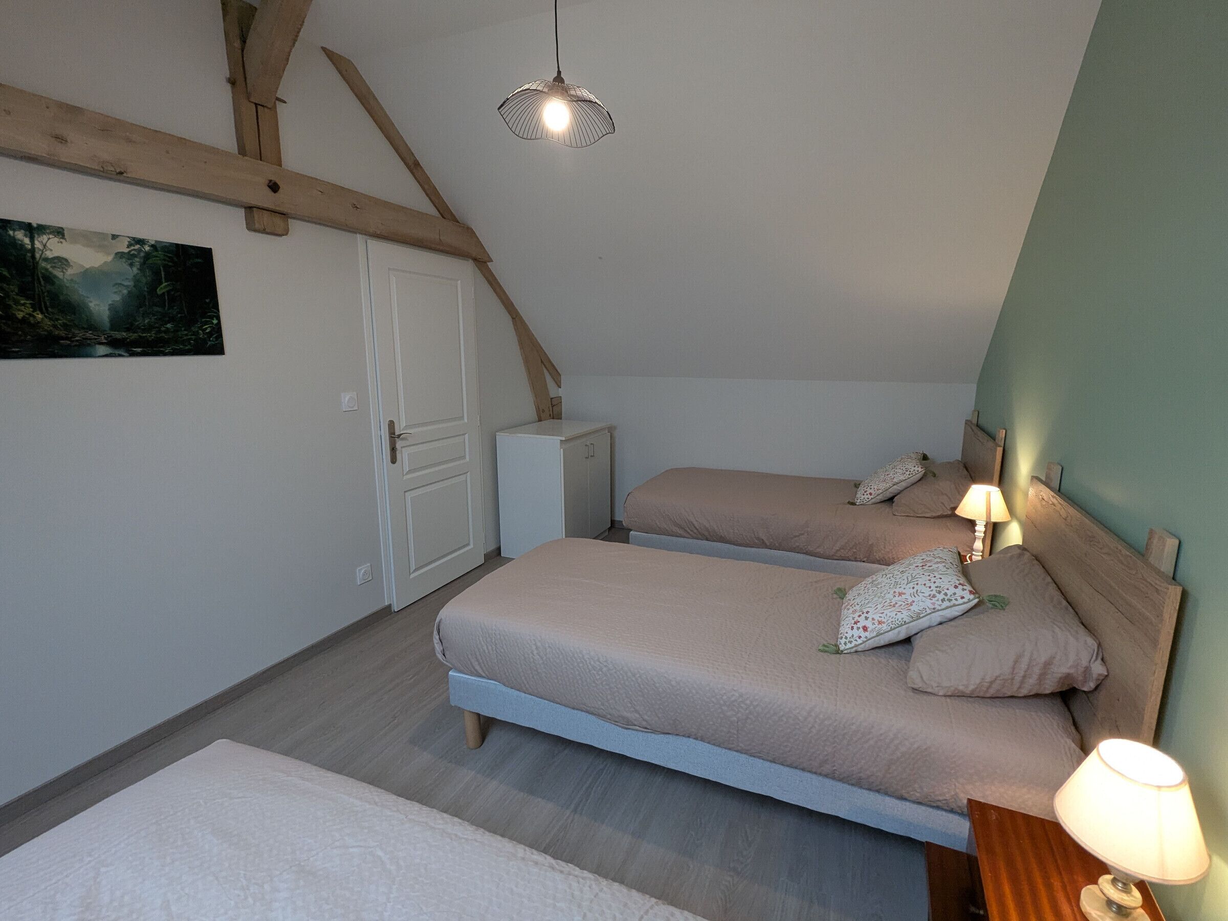 Un dormitorio con dos camas, un mueble pequeño, un cuadro en la pared y un techo inclinado.
